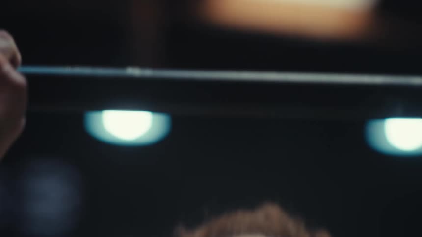A woman with curly hair looks upward with focus while performing overhead presses with a barbell in a gym the camera uses tight lowangle shots to capture her exertion and the movement of the weight rack
