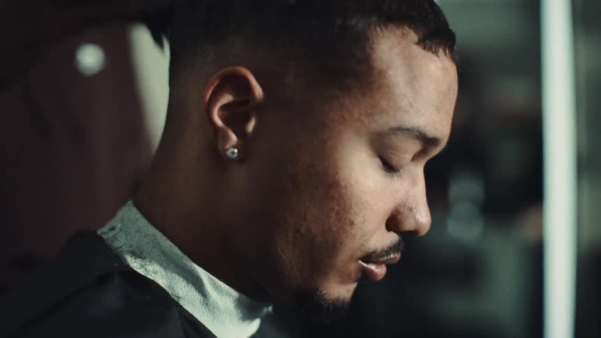 A young man getting a haircut at a hair salon from a male barber at midday