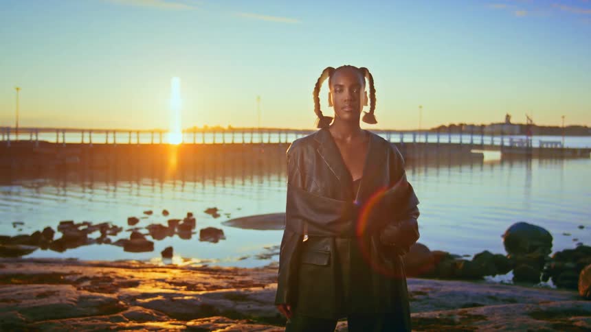 A female model wearing a black jacket posing on the shoreline at sunset
