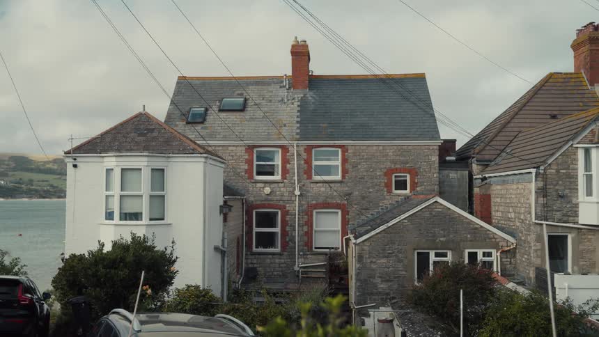 House with a repaired roof stands on shore under an overcast sky