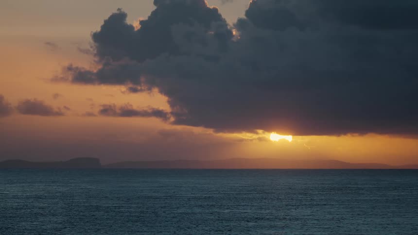 Dark cloud partially blocks the sun shining from a red sky onto a foggy coastal area
