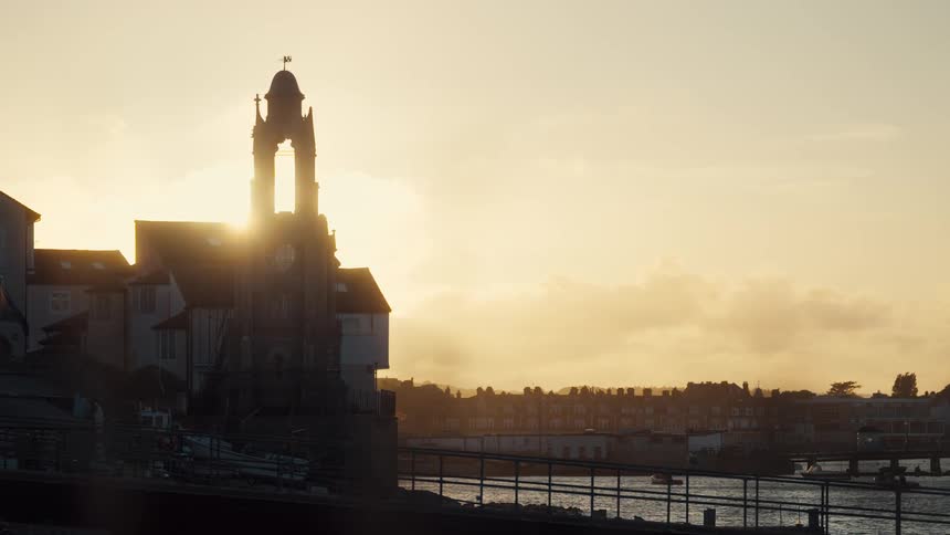 Historic bell tower next to historic buildings on the waterfront of a city outdoors during dusk or dawn