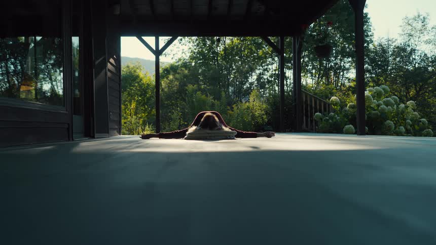 A woman lying on a yoga mat stretching her arms outward on her stomach surrounded by green vegetation at midday