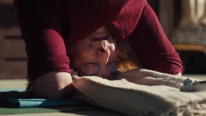 Adult woman wearing a red sweater doing a headstand yoga position in a porch outdoors during day time