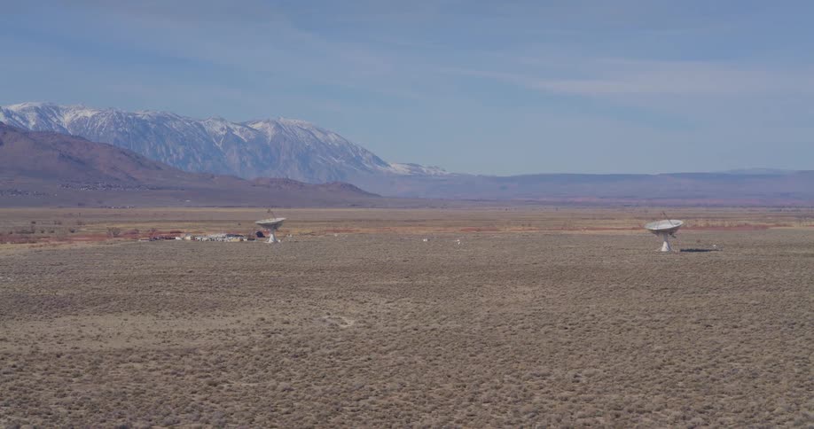 Satellite dishes scattered across an arid plain with snowcapped mountains in the background