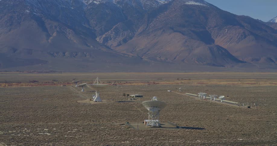 Group of satellite dishes spread across an arid plain with a mountain range in the background