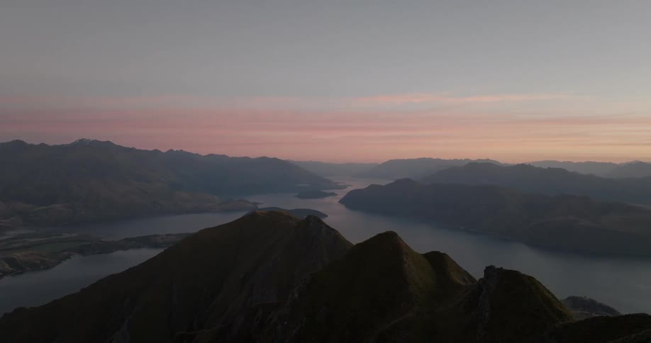 Peak of a mountain surrounded by a lake and other mountains outdoors during dusk or dawn