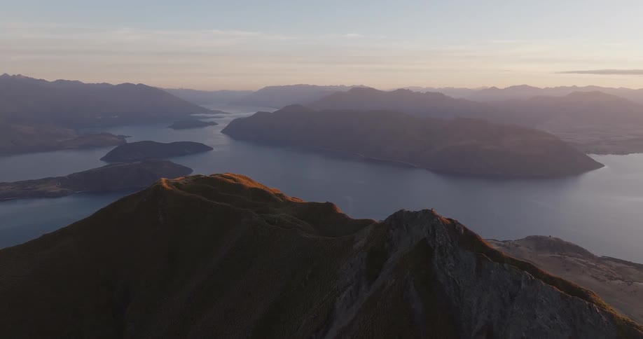 Sunlit mountain ridge with a winding lake between mountain ranges in the background