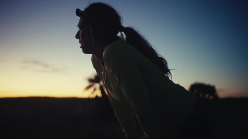Woman runs at dusk wearing a headlamp in an open environment