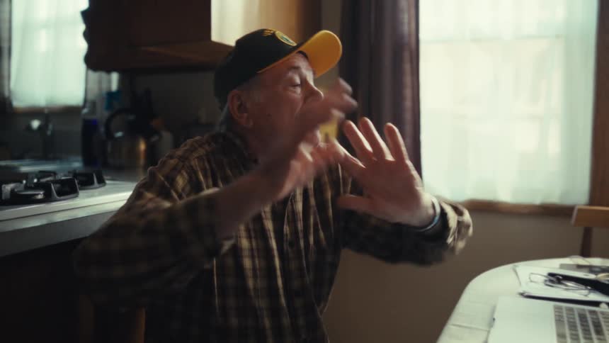 Man sitting at a table with a laptop computer moving his arms in dance moves and smiles in celebration