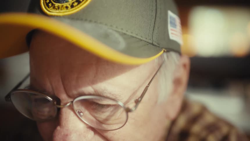Elderly man puts on glasses while seated indoors