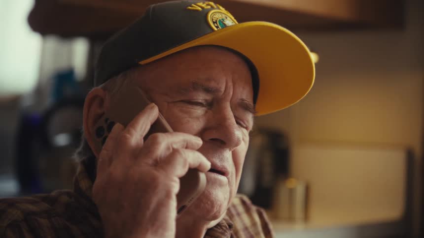 Elderly man talks on a cellphone while seated indoors