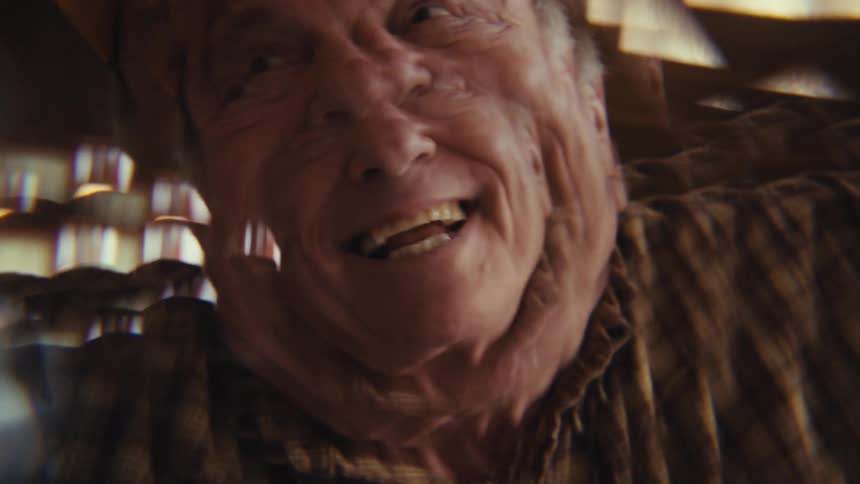 An elderly man laughing excitedly indoors wearing a baseball hat at midday