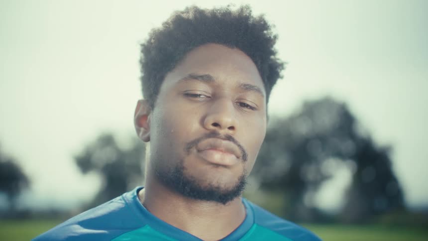 Young adult black man in sports clothing standing on a field outdoors during day time