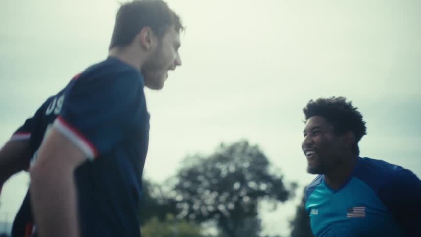 Two soccer players celebrate on a field with one in a blue jersey raising his arms for a high fivethey successfully clap hands and share a joyful moment together against an overcast sky