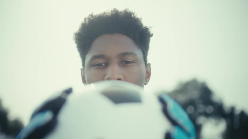 Goalkeeper in blue uniform holds soccer ball in front of face