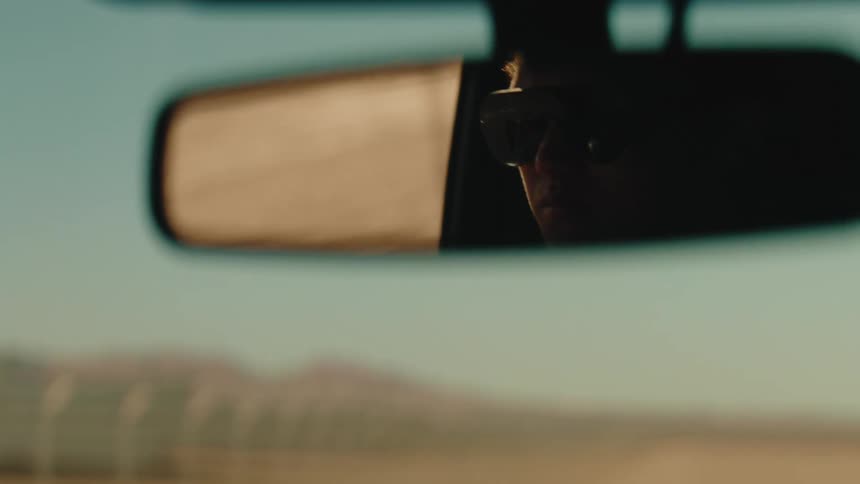 Reflection of a person wearing sunglasses in the rear view mirror of an automobile traveling by mountains