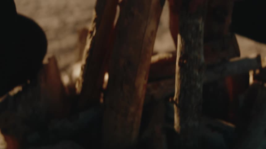 Hands carefully arrange wooden logs on sand to start a campfire