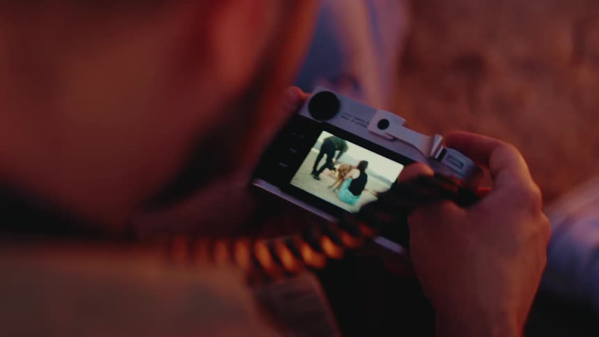 A person holds a silver digital camera likely a leica and scrolls through photos on the rear lcd screenthe images displayed on the screen show a woman and a dog together on a beach during the golden hour