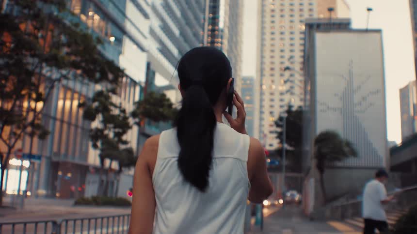 Woman with tied hair walking and talking on phone in modern urban area