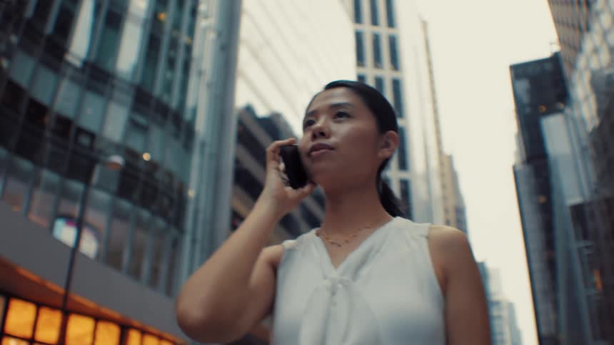Woman in white blouse on phone in urban street surrounded by modern buildings