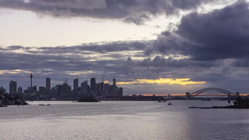 Sydney skyline at anoitecendo with sydney harbour bridge and sydney opera house illuminated under cloudy sky reflected on the bay