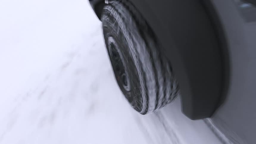 A vehicles tire spins driving through deep snow kicking up white flakes