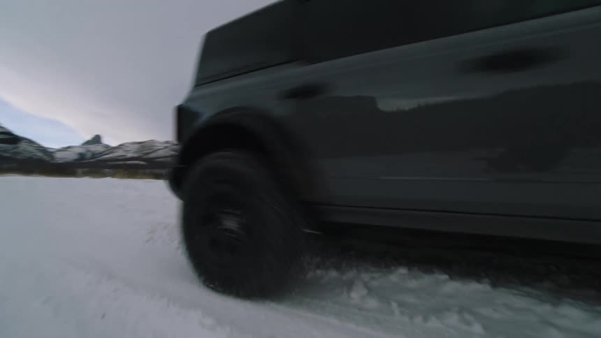 Black suv driving on a snowcovered road with mountains in the background