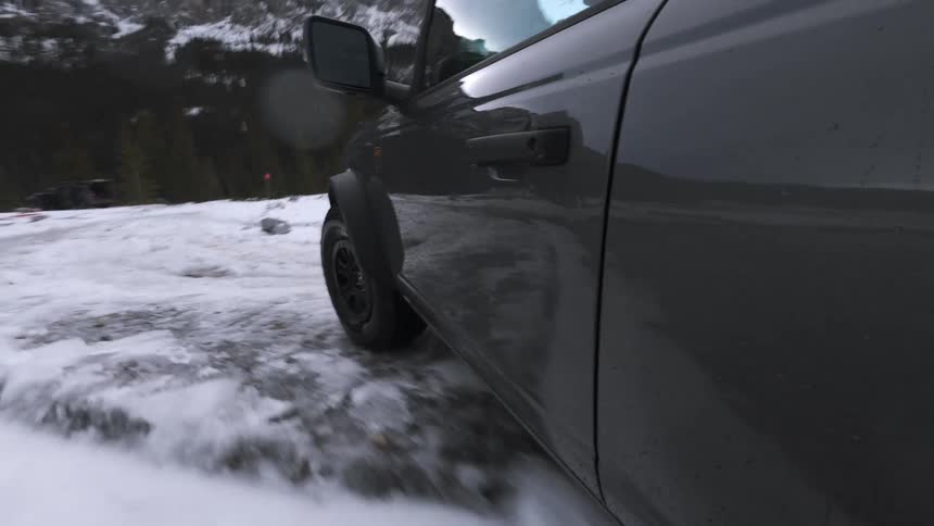 Car splashes through water on a snow and ice covered road through a forested mountain valley