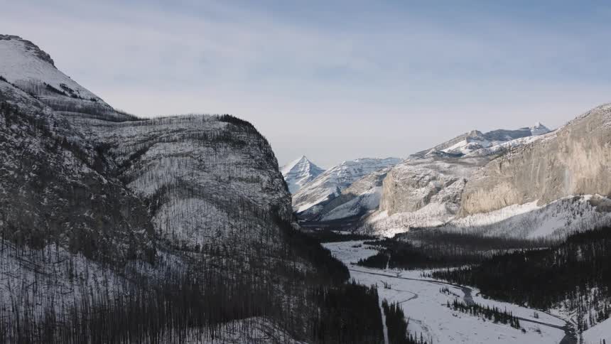 Streams flow through a valley between forested mountains on a cloudy winter day