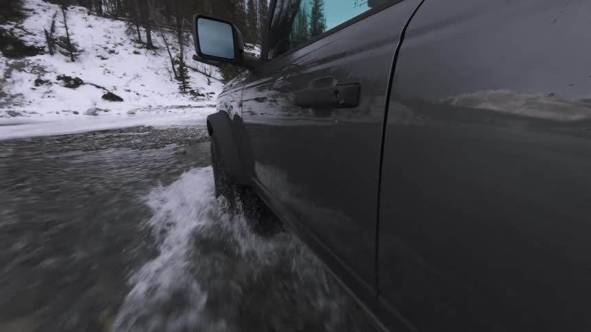 Car drives through flooded section of road with snow along the edges