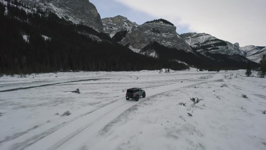 Truck traveling through the snow covered terrain between forests and mountains