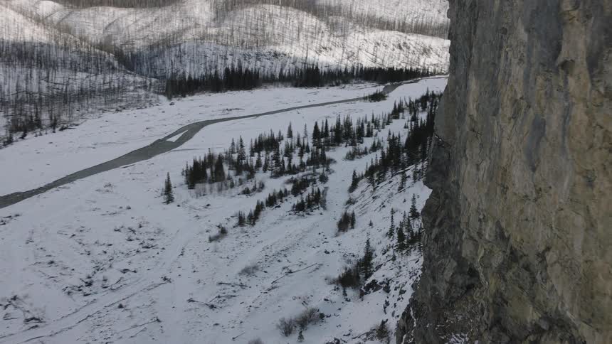 Snowcovered valley with winding river and rocky cliff on the side