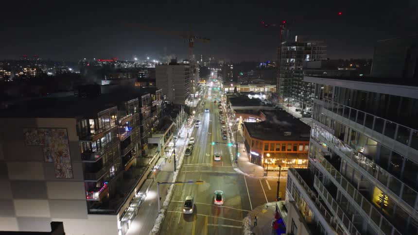 Lights illuminate a downtown street as traffic moves past buildings on a winter night