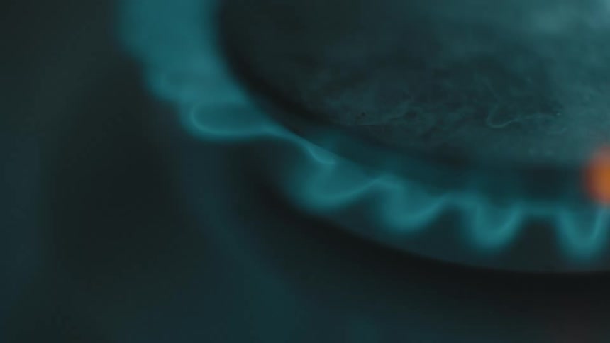 A close view shows orange sparks and small flames flickering as a blue gas fire ignites under a circular black burner on a metal stove top in a dark room