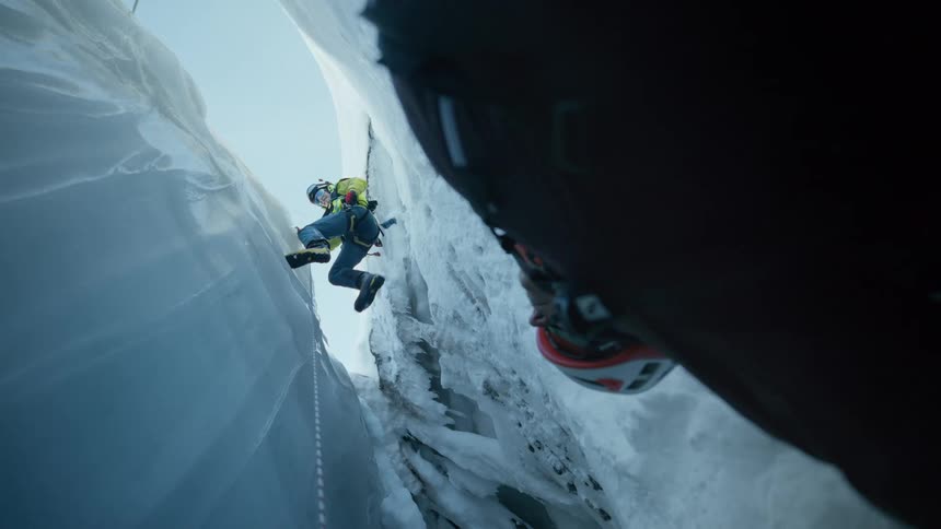 The man is descending on a rope down the icy cavern