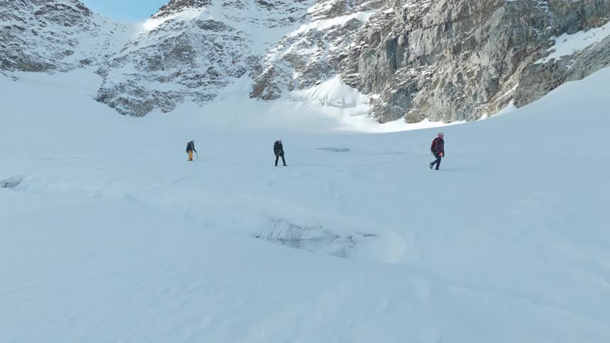 Three people walk across a snowcovered surface between rocky mountains