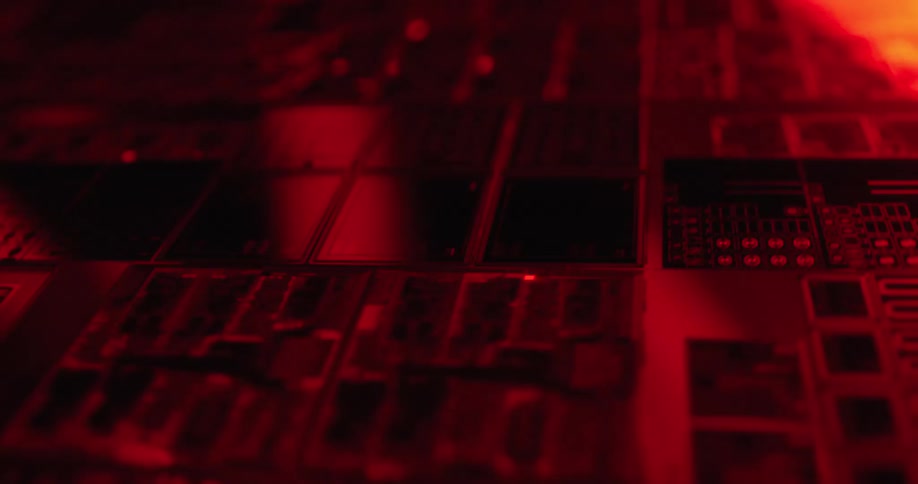 Closeup of an audio mixing console with faders and buttons illuminated in red tones