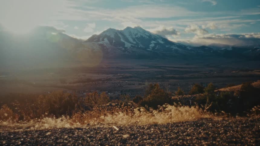 A vast stretch of barren land in the wilderness with a mountain range in the background at sunset