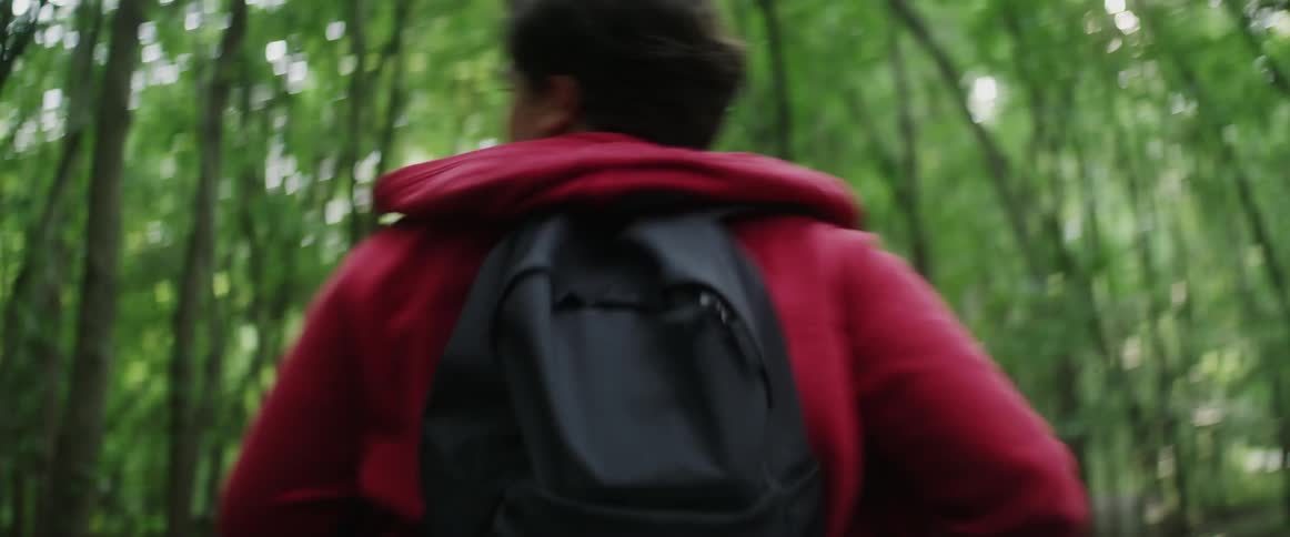 Man wearing backpack is running through trees in forest
