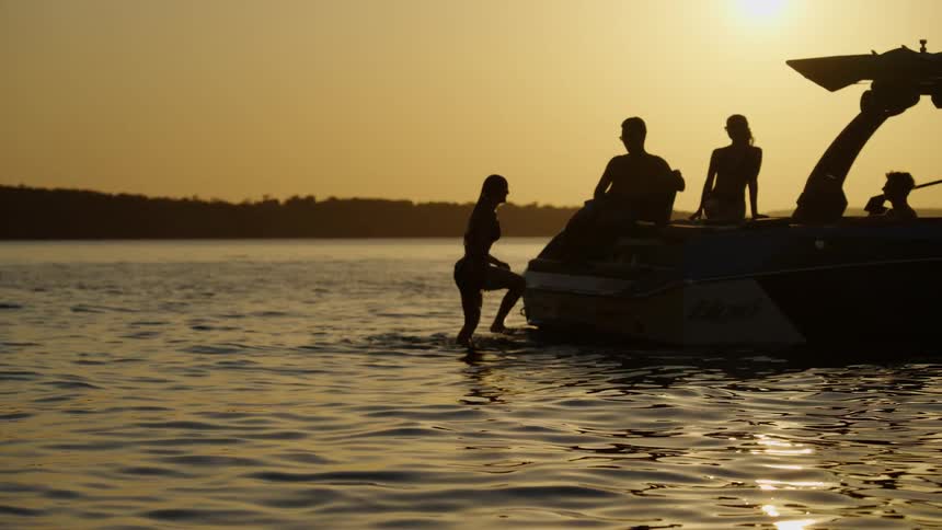 Silhouettes of people beside a boat on a lake at sunset