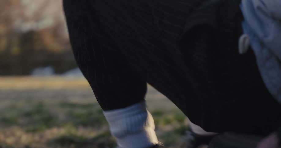 A close view of a man wearing a grey vest and black sneakers stands up from a tire in a grassy yard as the bright sun creates a warm atmosphere during a late afternoon workout