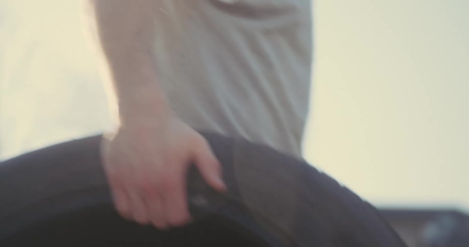 A man carries and tosses a heavy black tire in grass