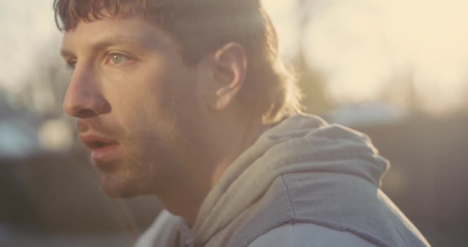 Man wearing a hoodie looks into the distance under golden sunset light