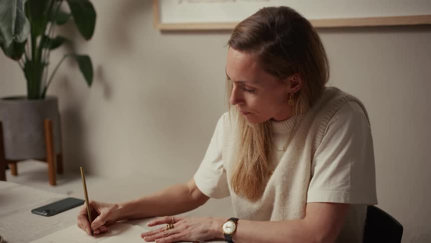 Woman writes in notebook while drinking from mug