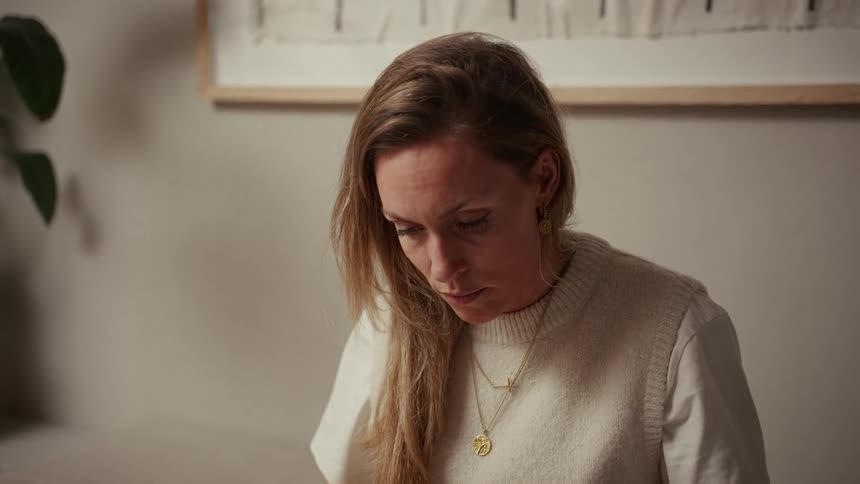 Young adult woman wearing a woolly vest sitting and reading with a nervous facial expression indoors