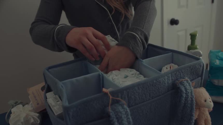 A person carefully organizing a blue multicompartment felt caddy with baby suppliesthey pick up a stack of diapers and place them neatly into one of the central sections alongside other nursery essentials