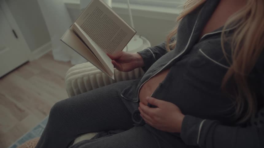 Pregnant woman sitting and reading a book while resting her hand on her belly