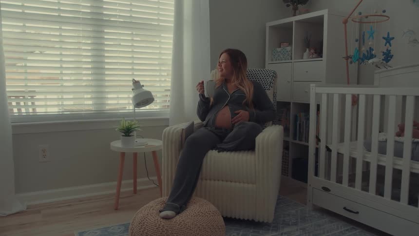 Pregnant woman in a childs room with an armchair side table and white crib