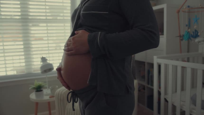 Pregnant woman standing with hands resting on her belly in a lit room